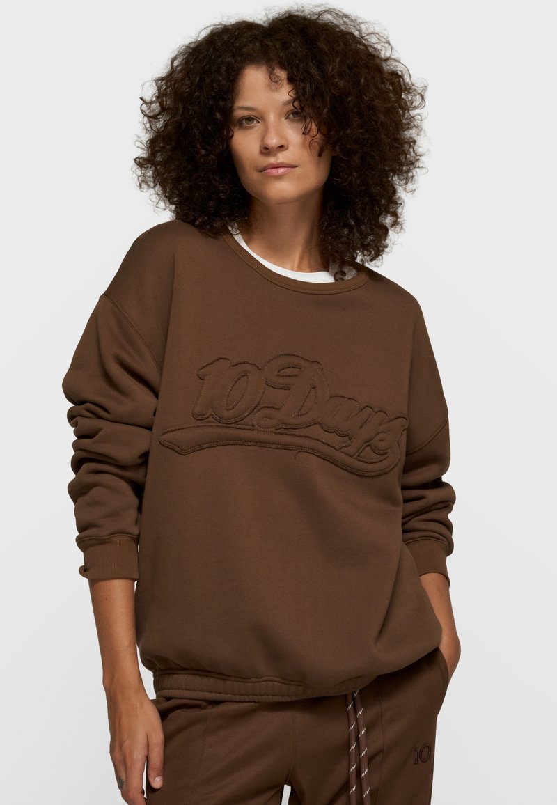 Sweatshirt marron avec logo 10 Days en broderie ton sur ton, coupe décontractée, poignets côtelés et encolure ronde, associé à un pantalon marron assorti.