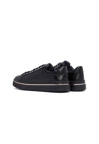 Sneaker in pelle nera con texture liscia, punta arrotondata e design con lacci. Presenta un accento metallico a contrasto sulla suola.