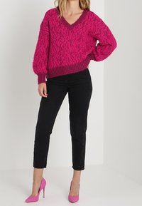 Fuzzy, leuchtend pinker Strickpullover mit V-Ausschnitt und geripptem Saum, kombiniert mit schwarzen schmalen Jeans und pinken High Heels.