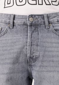 Jeans en denim gris avec fermeture à bouton et à glissière, dotés de poches avant et d'une coupe classique. La texture semble lisse avec un léger délavage.