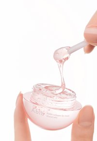 Masque lèvres au collagène dans un pot transparent rose, présentant une texture lisse et brillante. Applicateur cuillère soulevant un gel avec des gouttelettes. Étiquette visible.