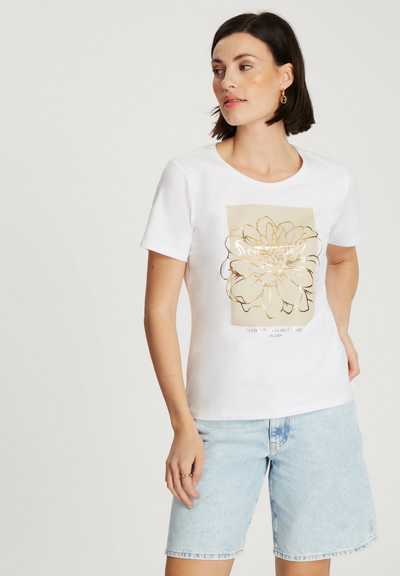 Biała koszulka z krótkim rękawem z złotym graficznym wzorem kwiatowym na jasnobeżowym tle. Miękka tkanina, okrągły dekolt i luźny krój.