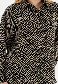 Camicia nera e beige con motivo a strisce di zebra, maniche lunghe, chiusura con bottoni e un tessuto morbido e testurizzato.