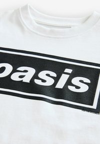 Hvid bomulds T-shirt med et sort rektangulært mønster, der har ordet "oasis" i fed skrift, struktureret tryk på stoffet.