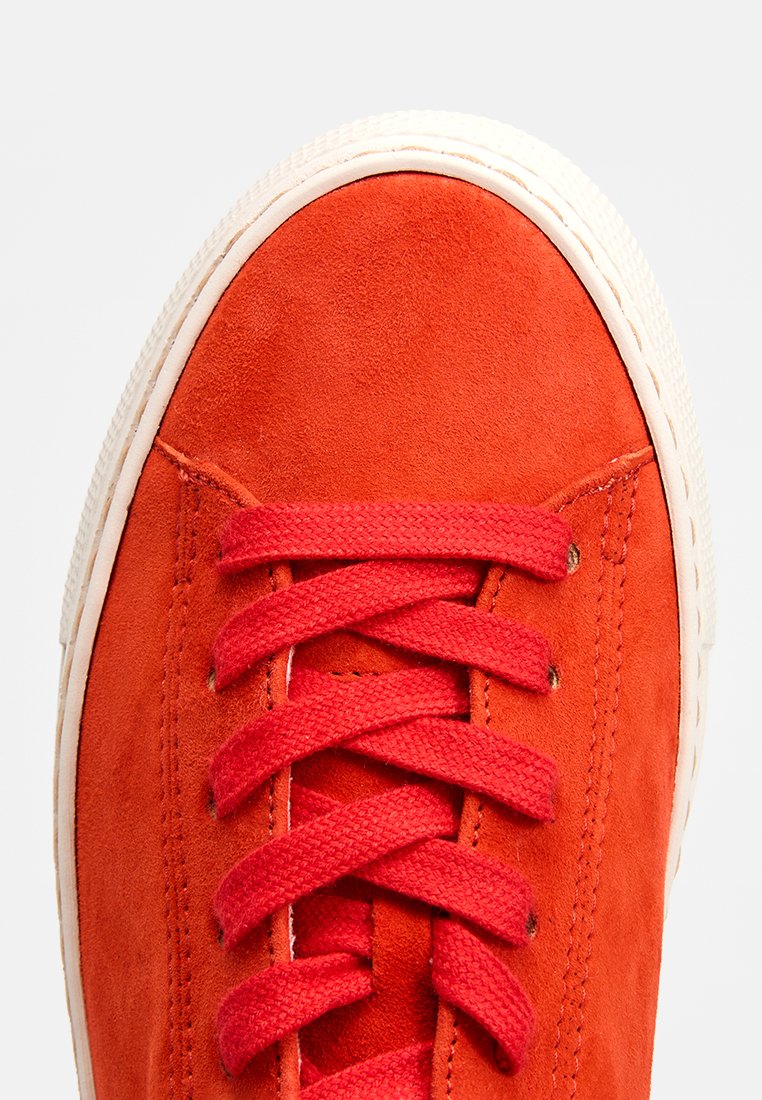 Rote Wildledersneaker mit passendem Schnürsenkel, weißer Gummisohle, runder Zehenpartie und kontrastierenden Nähten. Glatte Textur mit einem sauberen Finish.