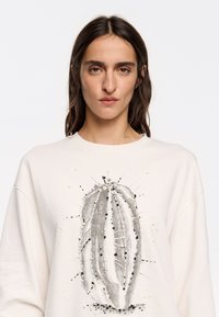 Sudadera color crema con ilustración de un cactus adornada con intrincados detalles de cuentas y lentejuelas, con un corte relajado y textura suave.