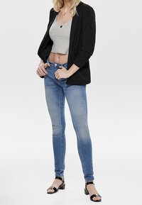 Blazer negro, top corto gris y jeans ajustados azul claro. Sandalias negras con una tira brillante. Texturas suaves, diseño ajustado.