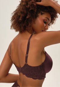 Burgundowy biustonosz koronkowy z gładkiego materiału, z wsparciem drucianym, regulowanymi ramiączkami oraz zapięciem na haftkę, ozdobiony misternym kwiatowym wzorem.