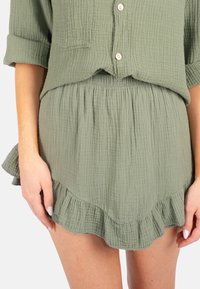 Ensemble en coton vert composé d'une chemise et d'une jupe avec un tissu texturé, une fermeture à boutons et un ourlet froncé sur la jupe. Design décontracté.