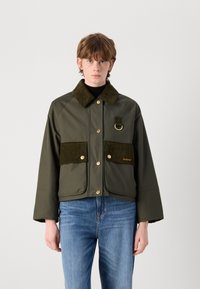 Olijfgroene cropped jacket met gouden knopen, corduroy kraag, twee voorzakken en een ringdetail. Zachte textuur met een modern design.