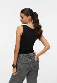 Top nero senza maniche abbinato a jeans grigi a vita alta. L'outfit presenta una silhouette aderente e un tessuto texture per il comfort.