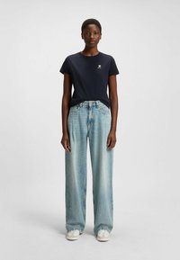 Laivastonsininen crew-neck t-paita sydängraafikalla, yhdistettynä vaaleansinisiin leveälahkeisiin farkkuihin. Valkoiset lenkkarit viimeistelevät asun.