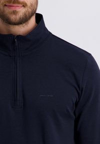 Donkerblauwe pullover met een ritskraag, voorzien van een zachte textuur en een subtiele geborduurde logo op de borst.