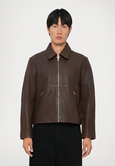 Veste en cuir marron avec une finition texturée, fermeture éclair et deux poches latérales. Présente un col et une silhouette courte.