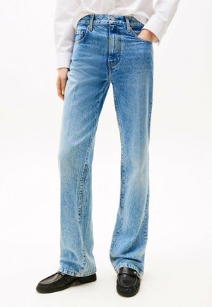 Light blue denim jeans with a high waist, wide leg, and faded finish, featuring five pockets and standard button closure. Paired with black loafers.