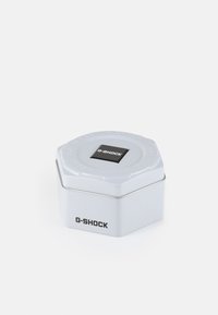 G-SHOCK hexagonal tin, white metallic finish, black logo on top, smooth texture, sliding lid, compact design for storing items.