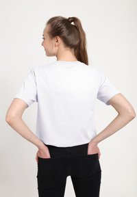 Bílá bavlněná tričko s krátkým rukávem, kulatým výstřihem a volným střihem, v kombinaci s černými džíny se zadními kapsami.