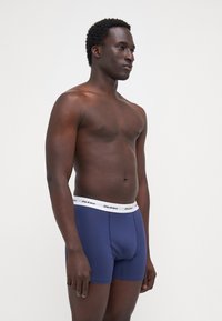 Marineblaue Boxershorts aus weichem Stoff, mit einem weißen elastischen Bund, der das "Dickies"-Logo trägt. Glatte Textur und reguläre Passform.