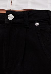 Black denim jeans featuring a silver button closure with the brand name "Bershka," front pockets, and a straight-leg design.
