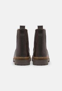 Bottines en cuir marron avec une finition lisse, des détails cousus et des languettes à l'arrière. Semelles en caoutchouc épaisses pour une meilleure adhérence.