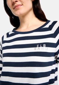 Langärmliges Hemd mit marineblauen und weißen Streifen und einem gerippten Halsausschnitt. Verfügt über ein kleines silberfarbenes Logo "ELB SAND" auf der Brust. Weicher Stoff.
