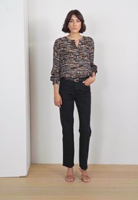 Printed blouse in dark tones with button front, long sleeves, and elastic cuffs. Paired with black slim-fit pants and flat sandals.