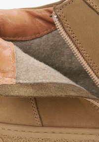 Tegen goudbruin leren schoenen met een zachte beige fleece voering, voorzien van een ritssluiting en contrasterende stikseldetails. Platte zool en gestructureerde afwerking.
