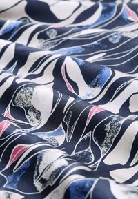 Tissu ondulé avec un fond marine et des motifs abstraits en blanc, bleu et rose. Texture lisse avec des tons et des formes contrastés.