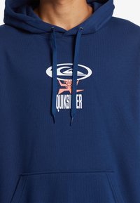 Sudadera con capucha azul marino fabricada en material suave, con un bolsillo tipo canguro en la parte frontal y un logo gráfico en blanco y rosa en el centro.