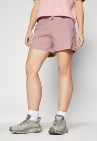 Ljusrosa shorts med dragsko i midjan; mjukt, lättviktsmaterial. Bärs med grå vandringsskor och vita strumpor.