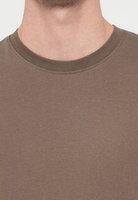 Rjava majica z okrolim izrezom iz gladkega, raztegljivega blaga z oprijeto obliko in vidnimi detajli šivov okoli izreza.