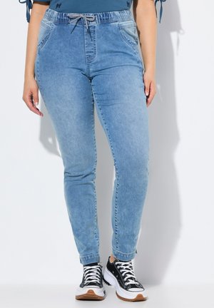 Helle blaue Denim-Jogginghosen mit einem Kordelzugbund, Seitentaschen und schmalem Schnitt, kombiniert mit schwarz-weißen Sneakers.