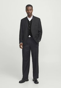 Schwarzer Anzug mit Ein-Knopf-Sakko, schwarzer Weste und weißem Hemd. Gerade geschnittene Hosen und schwarze Schuhe mit glatter Textur.