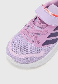 Basket de sport violette avec tige en maille, lacets texturés, sangle Velcro et accents rose clair. Semelle courbée pour plus de flexibilité.
