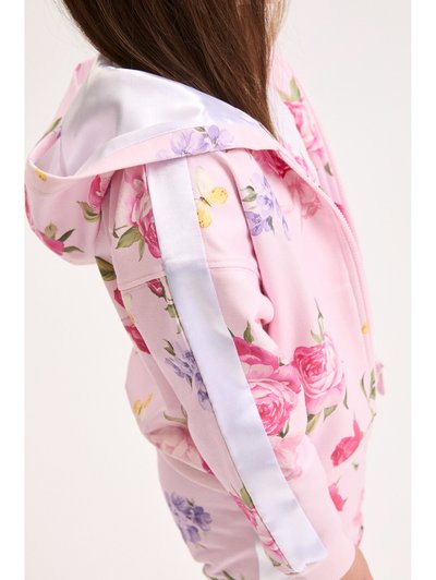 Παιδί που φοράει ροζ φλοράλ φούτερ με κουκούλα και ταιριαστά σορτς με λευκή σατέν ρίγα στα μανίκια, δείχνοντας πλευρικό προφίλ και μακριά καστανά μαλλιά.