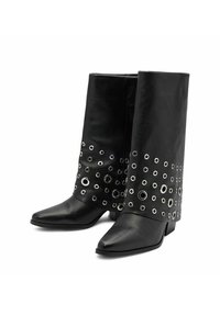 Bottines en cuir noir avec un talon plat, présentant un bout pointu et un détail distinctif en œillets argentés autour de la section mi-mollet.