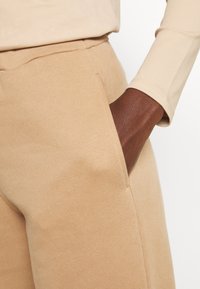 Beżowe spodnie z bawełnianej mieszanki z kieszenią boczną, miękka tekstura, luźny krój i widoczny detal w postaci szwów, połączone z pasującą bluzką z długim rękawem.