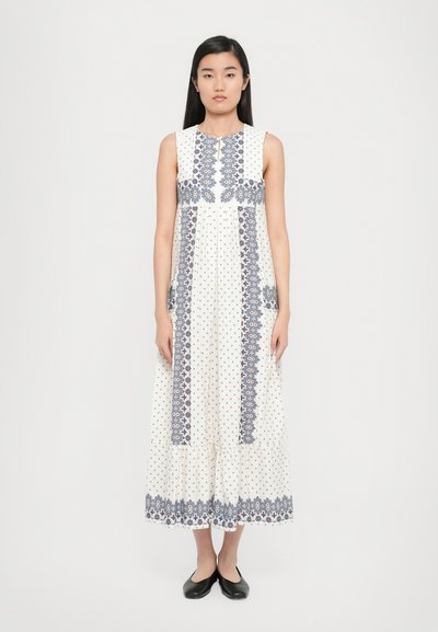 White maxi dress with blue floral patterns and dots, featuring a round neckline and a flared hem. Paired with black flat shoes.