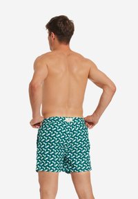 Costumi da bagno con elastico in vita, caratterizzati da un motivo geometrico verde e bianco. Tessuto morbido, lunghezza fino a metà coscia e tasche laterali.