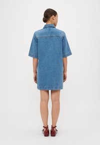Denimkleid mit kurzen Ärmeln, einem Kragen und einer lockeren Passform. Es hat einen hellblauen Farbton und reicht bis zur Mitte des Oberschenkels, mit sichtbaren Nähtelementen.