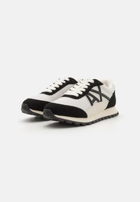 Black and white athletic shoes feature a mesh upper, suede accents, and a rubber sole with a textured pattern for grip.