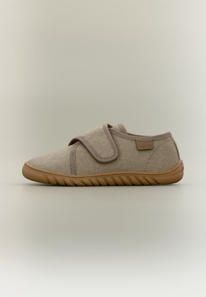 Chausson en tissu beige avec une large bande velcro unique et une semelle en caoutchouc marron texturée sur un fond neutre.
