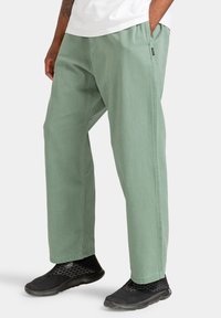Lichtgroene, ontspannen pasvorm broek van gestructureerd katoen, met een wijd uitlopende pijp en zijzakken, gecombineerd met zwarte mesh sneakers.