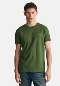 Groene katoen t-shirt met een ronde hals, korte mouwen en een klein gouden logo op de borst. Draagt met blauwe denim jeans.