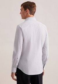 Camicia bianca con motivo geometrico nero, maniche lunghe, colletto appuntito e polsini abbottonati. Vestibilità sartoriale con orlo curvo.