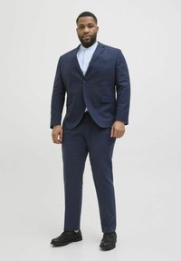 Marineblaues Anzug mit einem Ein-Knopf-Blazer und passenden Hosen. Darunter ein hellblaues Hemd und schwarze Schuhe. Glatte Textur.