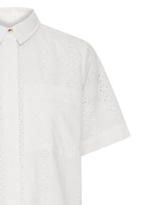 Balta īsroku krekls ar izšūtu ziedu acs rakstu, ar pogām priekšpusē un krūšu kabatu kreisajā pusē.