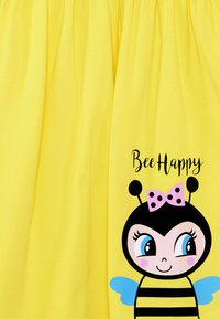 Gelber Stoff mit einem Cartoon-Bienen-Motiv, das schwarze Streifen, eine rosa gepunktete Schleife, blaue Flügel und den Text "Bee Happy" zeigt.