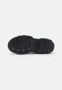 Suola di scarpa in gomma nera con un motivo a zigzag testurizzato, sezioni rinforzate e fori di drenaggio per trazione e stabilità.