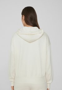 Hoodie aus weichem Creme-Stoff, mit einem lockeren Schnitt, gerippten Bündchen und Saum, sowie einer subtilen Textur und Nahtdetails.